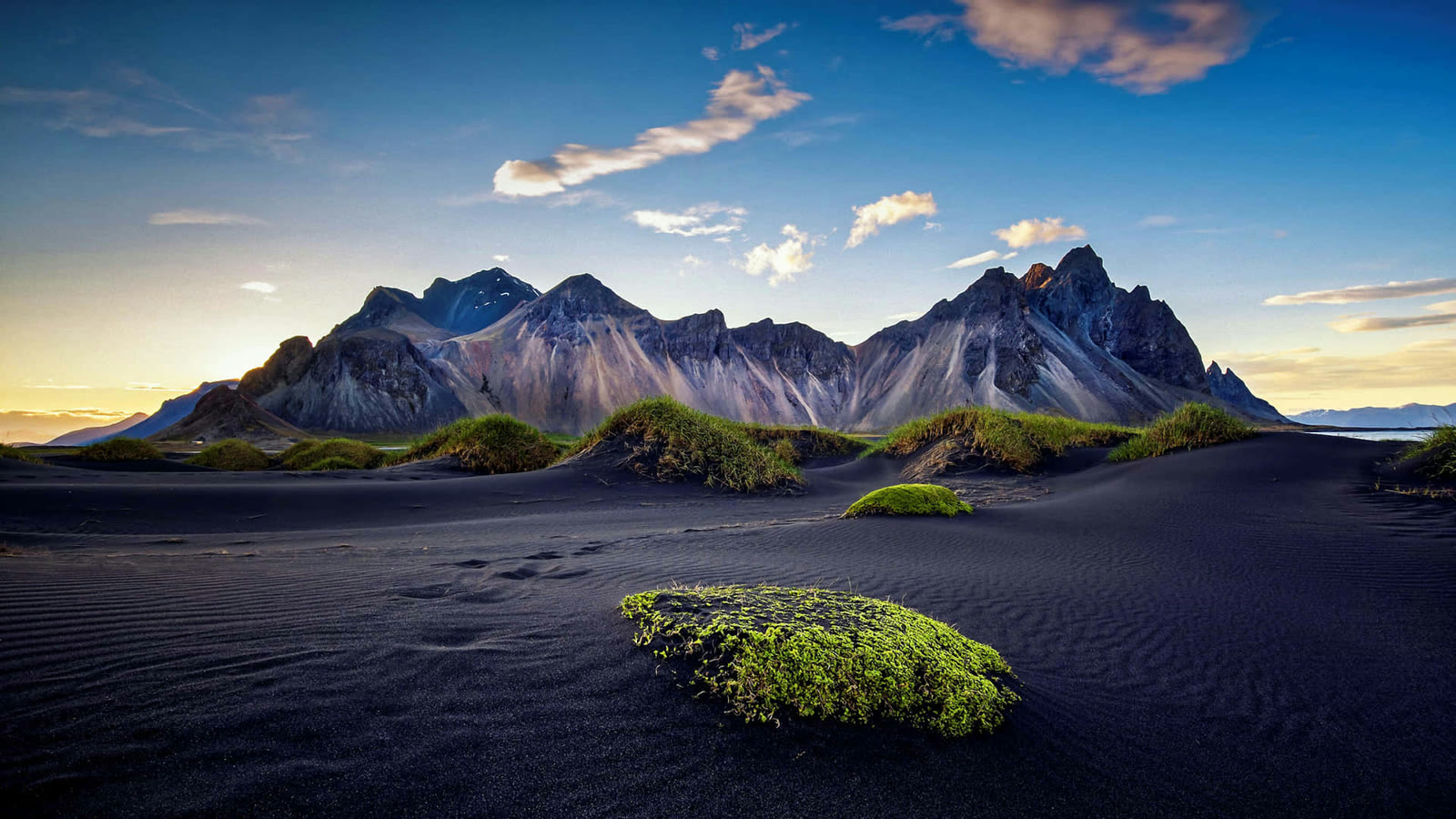 Green moss and grass on black sand below mountains